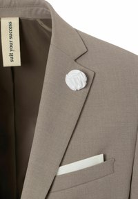 Lichtbeige blazer van een gestructureerde stof. Voorzien van een witte stof reversspeld en een contrast zakdoek die uit de borstzak steekt.