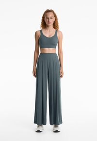 Teal tweedelige activewear set met een aansluitende crop top met brede banden en hoge taille, vloeiende broekspijpen. Zachte stoftextuur.