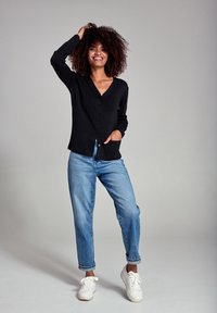 Sort v-hals cardigan med knaplukning og to forlommer, parret med lyseblå løse jeans og hvide sneakers.