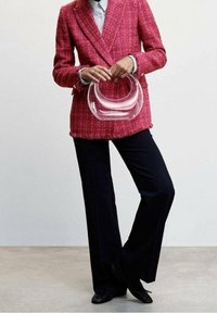 Vaaleanpunainen tweed-takki, jossa on purjehduksia, yhdistetty mustiin housuihin ja läpinäkyvään pyöreään laukkuun. Yksinkertaiset napit ja tyylikkäät kengät viimeistelevät ilmeen.