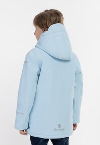 Chaqueta impermeable de color azul claro con capucha, que presenta mangas largas, un logo en la manga y un acabado suave y texturizado.