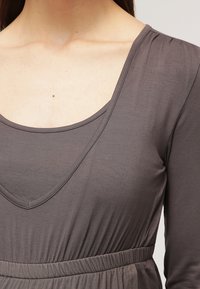 Gray long-sleeve top featuring a deep V-neckline, soft textured fabric, and an elastic waist. Simple, unembellished design.