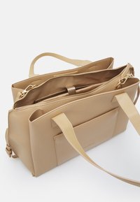 Beige leather tote bag with textured surface, dual handles, and a gold zipper. Features a spacious interior with multiple pockets.
