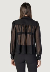 Blusa nera con tessuto trasparente sul retro, maniche a palloncino, polsini con bottoni e dettaglio arricciato lungo le spalle.