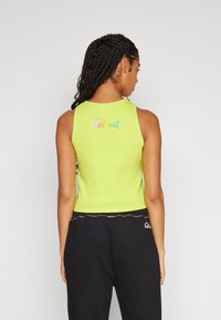 Neon groene geribbelde tanktop met geborduurde "Colucci" tekst op de achterkant. Gecombineerd met zwarte broek met een kleurrijke patroon tailleband.