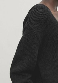 Schwarzer, gestrickter Pullover mit weitem Ausschnitt, strukturierter Stoff und langen Ärmeln. Das Design zeichnet sich durch lockere Maschen und eine entspannte Passform aus.