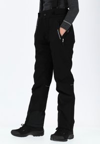 Pantalons de ski waterproof noirs avec des bretelles ajustables, poches latérales zippées et accents réfléchissants ; tissu texturé pour plus de durabilité.