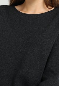 Pull noir à col rond, fabriqué dans un tissu doux et texturé qui présente un subtil éclat, mettant en valeur une surface lisse et une coupe généreuse.