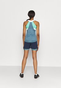 Top sportivo in teal e menta con un design a rete; abbinato a pantaloni corti navy con orlo decorato. Il modello è visto di spalle.