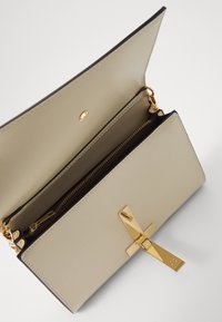 Portafoglio in pelle beige con dettagli in oro, dotato di una tasca con zip, chiusura a scatto e una tasca interna. Fodera tessurizzata.