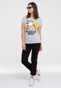 Grå bomulds t-shirt med et Snoopy-grafik, der har en regnbue og teksten "Dette er min... WEEKEND T-shirt", parret med sorte jeans og hvide sneakers.