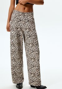 Pantaloni larghi a vita alta con stampa leopardata, realizzati in tessuto morbido, caratterizzati da macchie nere e marroni su uno sfondo chiaro.