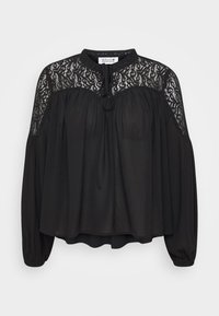 Blouse noire avec un empiècement en dentelle transparente, manches longues avec poignets élastiques et corsage froncé avec un lien au niveau du col.