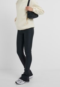 Felpa crema con tasca frontale, abbinata a leggings neri aderenti e scarpe da corsa grigie con accenti neri.