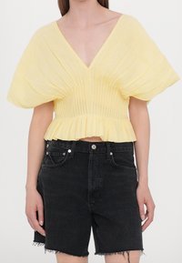 Top giallo corto con scollatura a V, pieghe testurizzate e maniche a sbuffo corte. Abbinato a pantaloni shorts in denim neri a vita alta.