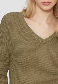 Pullover lavorato a maglia color verde oliva con scollatura a V, caratterizzato da un tessuto testurizzato e una vestibilità rilassata sulle spalle. Nessun ulteriore dettaglio visibile.