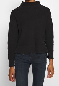 Suéter negro acanalado con cuello alto, hombros caídos y dobladillo ligeramente acampanado. Tejido texturizado y diseño minimalista.