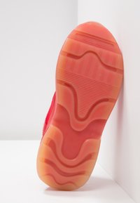 Semelle de basket rouge avec des motifs de bande de roulement courbes et linéaires, montrée à la verticale sur un fond blanc angulaire.
