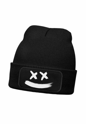 Schwarze, gestrickte Beanie-Mütze mit einem rechteckigen Aufnäher, auf dem ein weißes Smiley-Gesicht mit zwei Kreuzen abgebildet ist. Die Mütze zeigt eine gerippte Textur und sitzt eng an.
