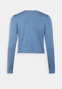 Pull court bleu à manches longues avec un col rond, vu de dos sur un fond gris clair uni.