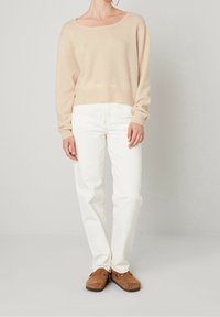 Béžový lehký pletený svetr se širokým lodičkovým výstřihem, kombinovaný s bílými džíny s vysokým pasem a rovnými nohavicemi a hnědými nazouvacími botami.