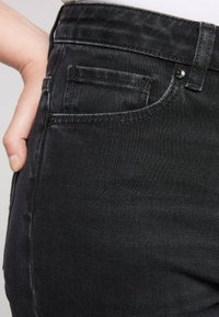 Jeans in denim nero con un design aderente, stile classico a cinque tasche e sottili dettagli di sbiadimento sulla trama del tessuto.