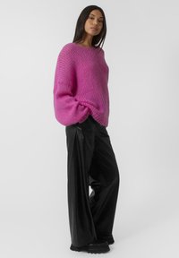 Maglione rosa oversized e morbido con scollo ampio e polsini a coste, abbinato a pantaloni in pelle nera larghi e stivali neri chunky.