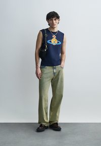 Μπλε ναυτικό αμάνικο πουκάμισο με γραφικό σχέδιο, συνδυασμένο με ανοιχτό πράσινο παντελόνι φαρδιάς γραμμής και σκούρα καφέ παπούτσια. Μαύρη τσάντα χιαστί.