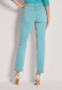 Turquoise broek met een rechte pijp, voorzien van achterzakken en een omgeslagen zoom. Gecombineerd met meerkleurige, patroonhooggehakte schoenen.