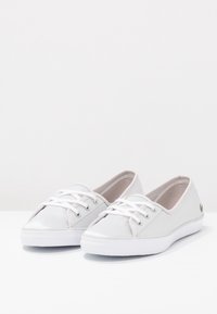 Une paire de baskets en toile blanches à tige basse avec des lacets blancs et des semelles en caoutchouc blanches sur une surface blanche.