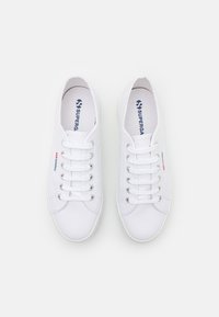 Hvite lerrets sneakers med rund tå, seks snøringshull og kontrasterende logo-akenter. Teksturert overflate og polstrede såler.