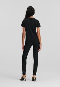 Maglietta nera in cotone a maniche corte con colletto tondo. Il retro presenta un logo stampato nella parte alta del collo. Abbinata a pantaloni neri attillati.