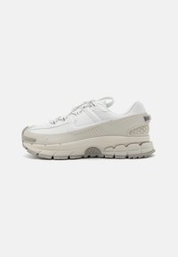Vita och beige låga sneakers med texturerad sula, mesh- och syntetöverdel, dragflik på hälen och vit Nike swoosh-logga på sidan.