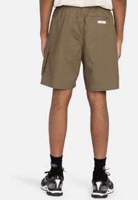 Khakifarbene Cargo-Shorts mit einem elastischen Bund, Seitentaschen, runden Stickdetails und einem lässigen Schnitt, kombiniert mit schwarzen Socken und Sneakers.
