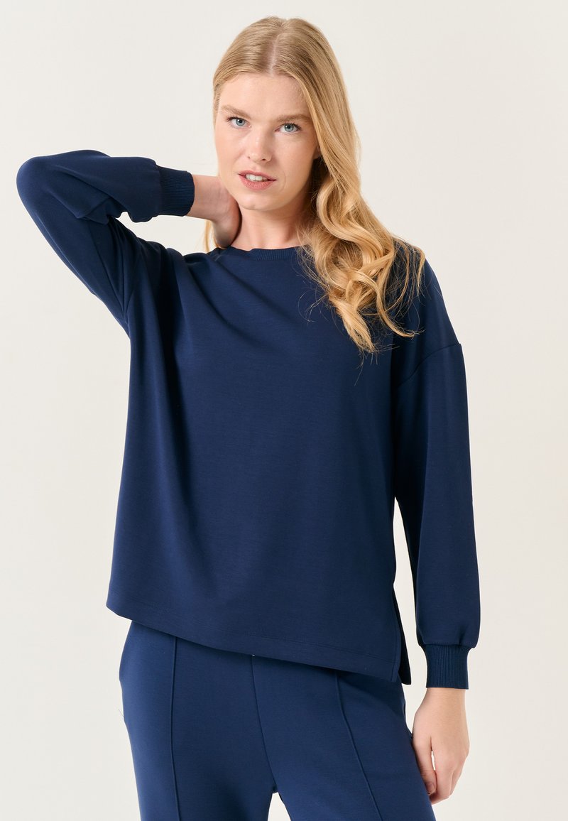 Camicia a maniche lunghe blu navy in tessuto morbido, con scollo rotondo, vestibilità relaxed e polsini a costine, abbinata a pantaloni coordinati.
