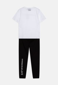 T-shirt blanc à manches courtes avec un logo dans le dos et leggings noirs unis avec du texte blanc sur le côté ; les deux en tissu doux.
