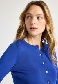 Cardigan blu lavorato a maglia con scollo rotondo, dotato di cinque bottoni d'argento e design aderente. Tessuto liscio, maniche lunghe.