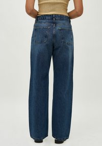 Široke denim hlače v temno modrem pralnem odtenku, z visokim pasom, elastičnim pasom in klasičnimi zadnjimi žepki. Mehka teksturirana tkanina.