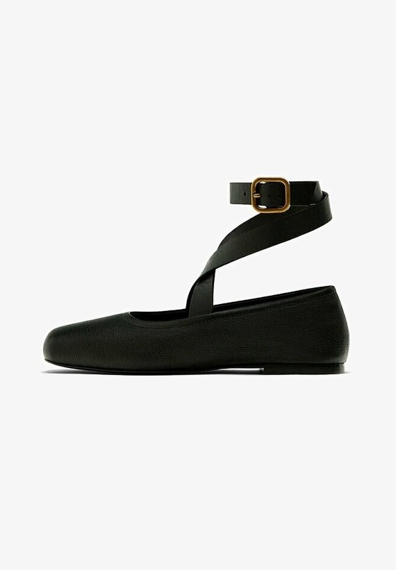 Ballerines en simili cuir noir avec une sangle de cheville présentant une boucle dorée rectangulaire ; bout rond et semelle plate.