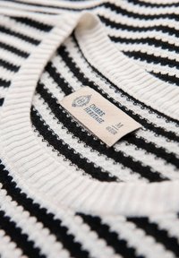 Suéter de punto a rayas blanco y negro con un cuello acanalado, que presenta una etiqueta que dice "Ombre Heritage" y tamaño M.