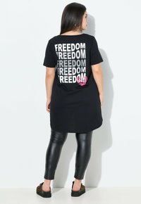 Zwarte tuniek t-shirt met de tekst "FREEDOM" in zilver en roze accenten, gecombineerd met zwarte leggings. Soepele stof en een relaxte pasvorm.