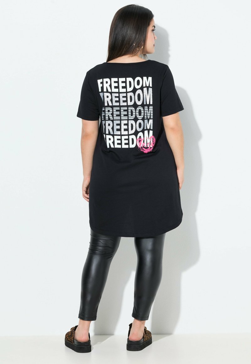 Schwarzes Tunika-T-Shirt mit dem Text "FREEDOM" in Silber und rosa Akzenten, kombiniert mit schwarzen Leggings. Glattes Material und lockere Passform.