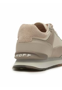 Lichtbeige sneaker met een gestructureerde suède hiel en een glad bovenwerk van synthetisch materiaal. Heeft een grijze zool en witte "HOFF" branding op de achterkant.