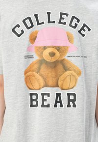 Gray cotton t-shirt featuring a teddy bear graphic wearing a pink hat. Text reads "COLLEGE BEAR" and "STUDY HARD NAP HARDER" in bold print.