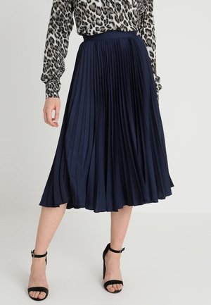 Granatowa plisowana spódnica midi wykonana z gładkiej tkaniny, z dopasowanym paskiem w talii, zestawiona z bluzką w panterkę i czarnymi szpilkami.
