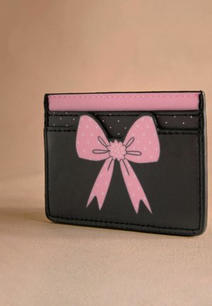 Porte-cartes noir avec un design de nœud rose. Comprend plusieurs emplacements pour cartes et une texture lisse. Accentué de pois blancs sur le nœud.
