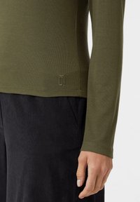 Oliwkowa koszula z długim rękawem o dopasowanym kroju, wykonana z miękkiego materiału. Z małym logo przy brzegu oraz czarne, gładkie spodnie.