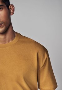 Sennepsfarvet T-shirt med korte ærmer lavet af glat bomuldsstof, som har rund halsudskæring og minimale syningsdetaljer.
