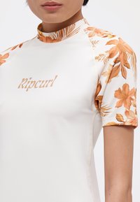 White rash guard featuring orange floral patterned sleeves and collar. Includes "Ripcurl" logo in a light orange shade on front. Smooth texture.