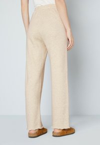 Beige wijde broek met een zachte textuur, elastische tailleband en rafelige zoom. Gemaakt met bruine instapschoenen.
